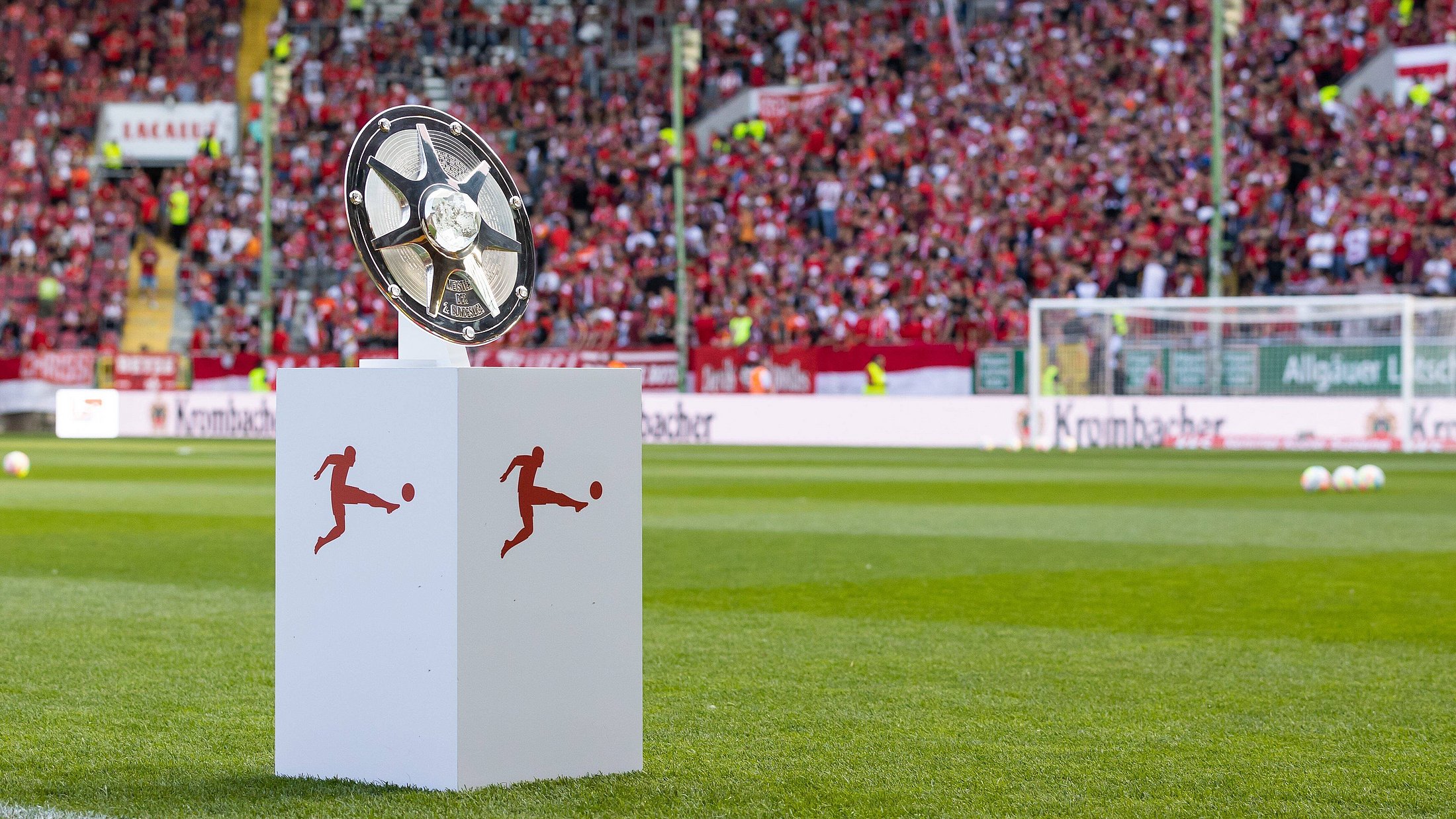 silberne Meisterschale der Bundesliga auf einem Sockel auf dem Rasen eines Fußballstadions