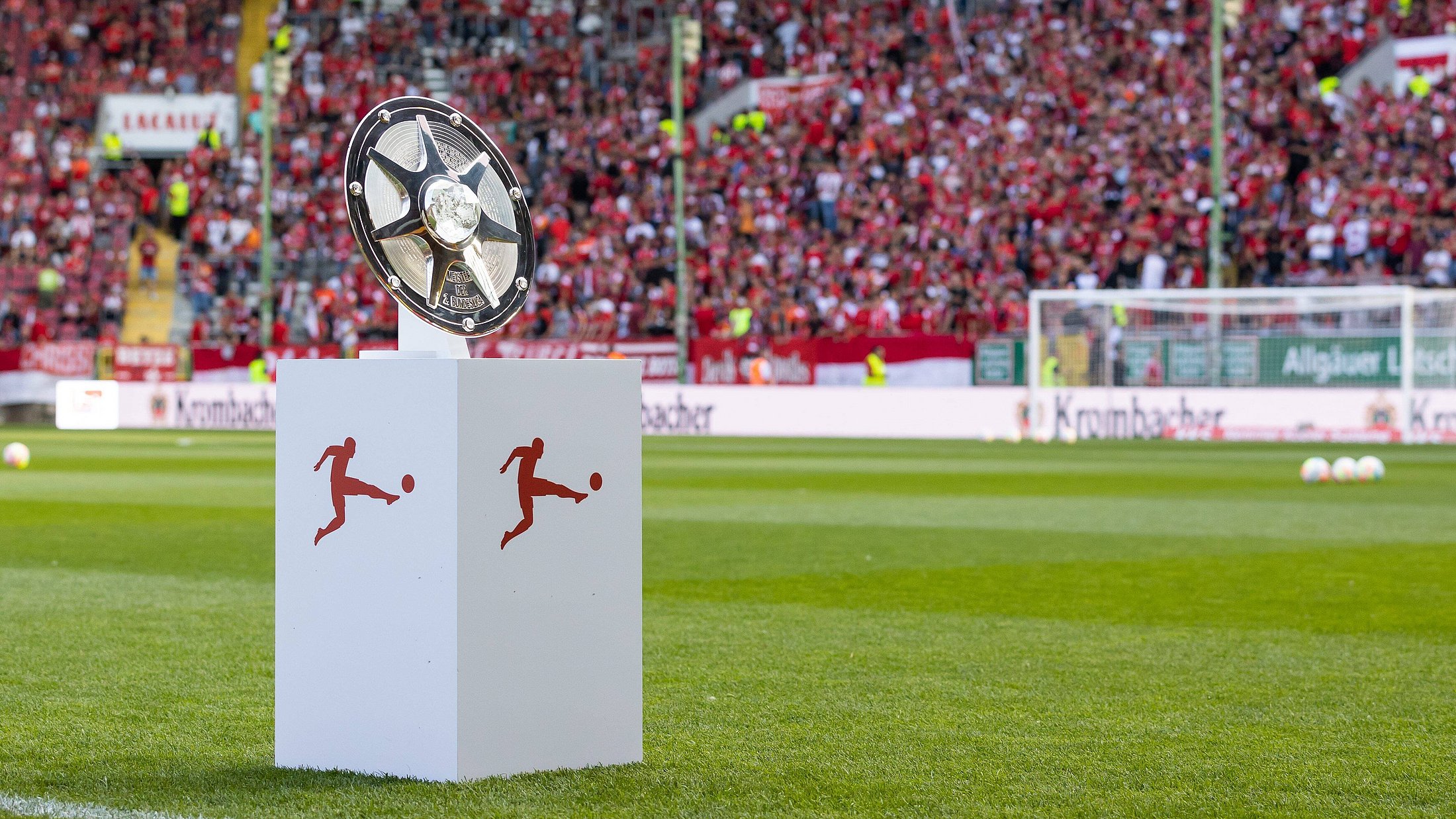 silberne Meisterschale der Bundesliga auf einem Sockel auf dem Rasen eines Fußballstadions