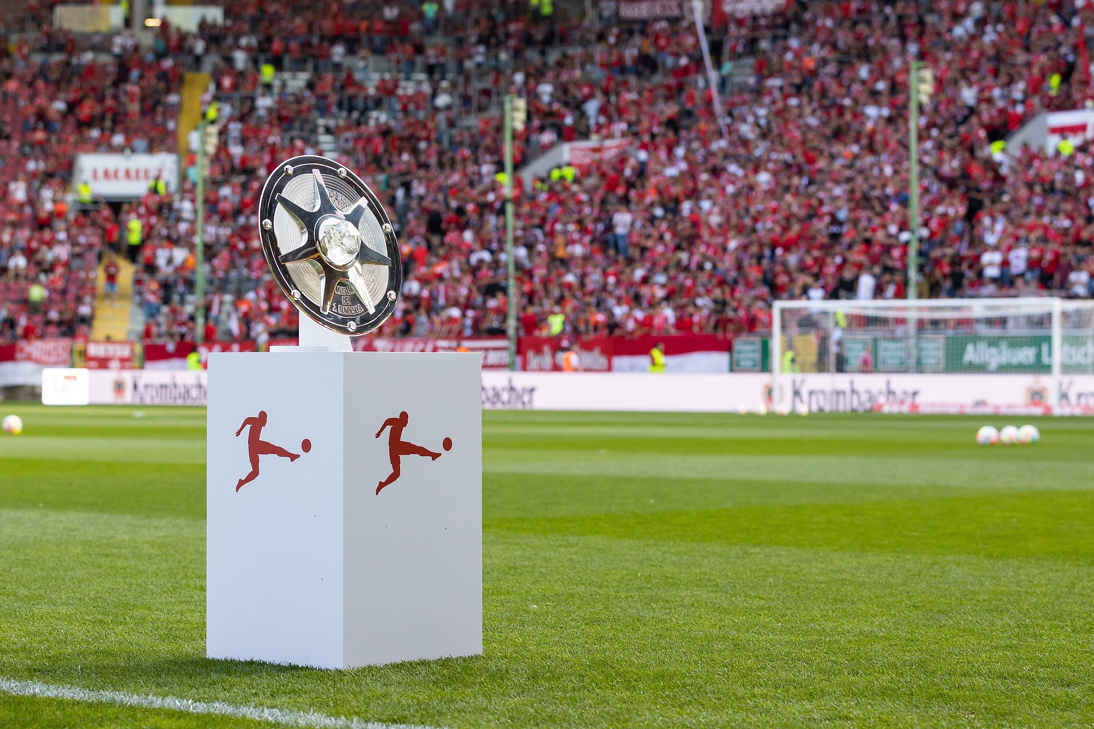 silberne Meisterschale der Bundesliga auf einem Sockel auf dem Rasen eines Fußballstadions