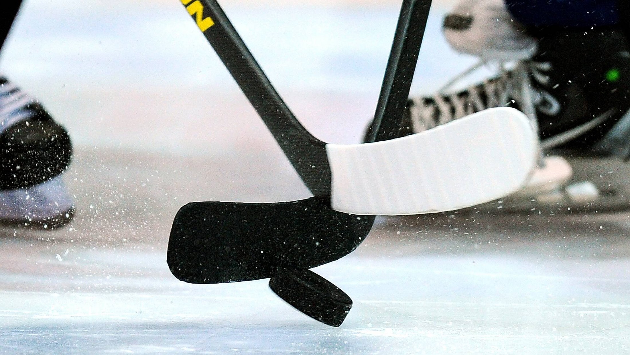 eine Eisfläche auf dem sich 2 Eishockeyschläger kreuzen, darunter der Puk