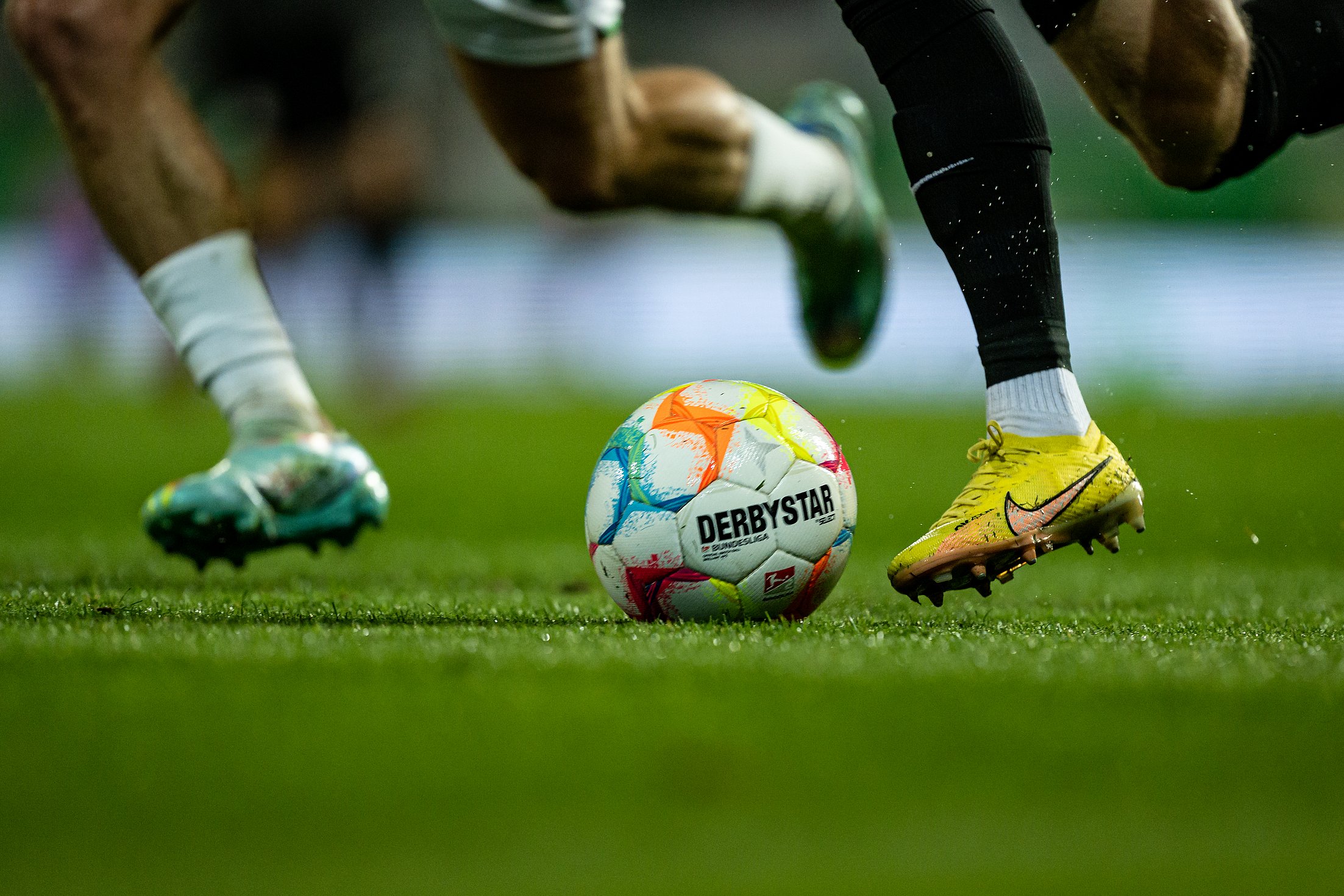 Ball auf dem Rasen. 2 Spieler laufen darauf zu 
