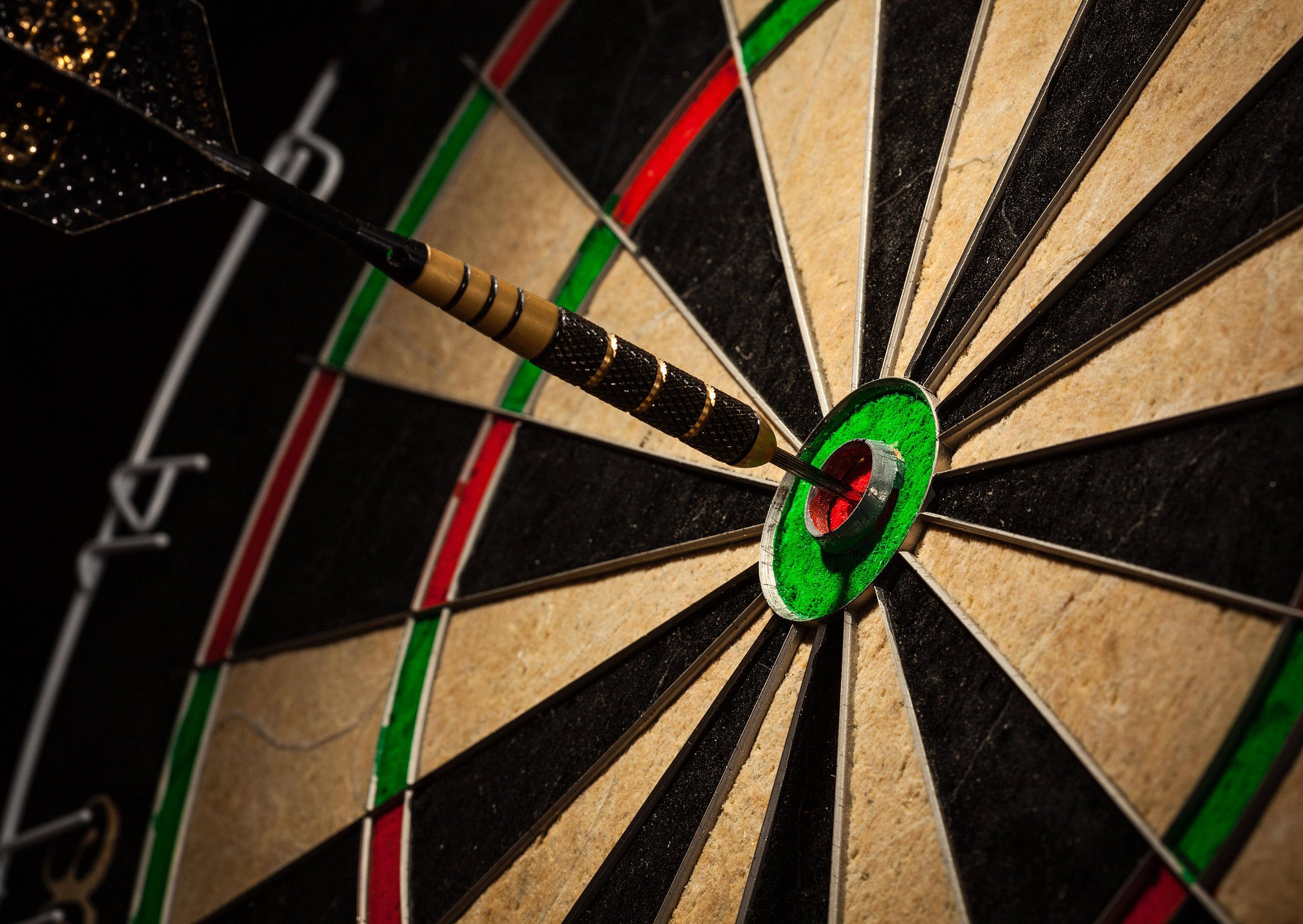 Nahaufnahme von einem Dartspfeil der im "Bulls-Eye" einer Dartsscheibe steckt